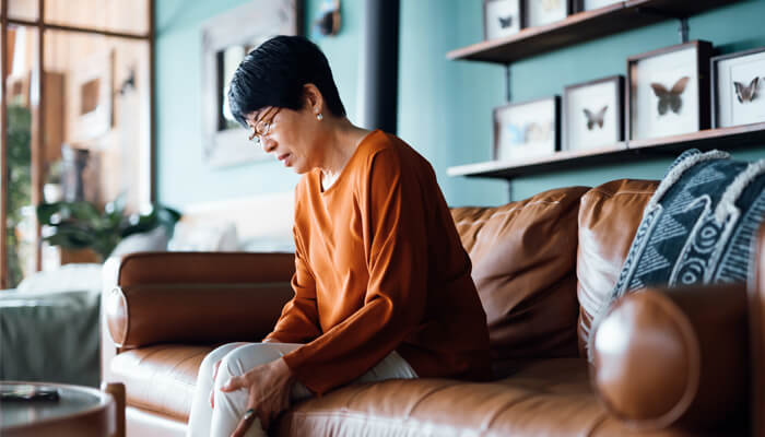 Woman sitting on a sofa looking down as she's massaging her leg