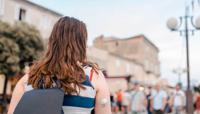 Back view of woman outdoors with a CGM on her upper arm & wearing a backback