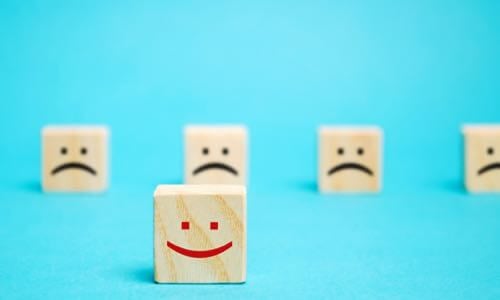 One wooden die with red smiley face in front & five wooden die with black frown faces in back