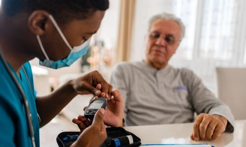 Diverse male health care professional showing a senior male patient how to test his blood glucose