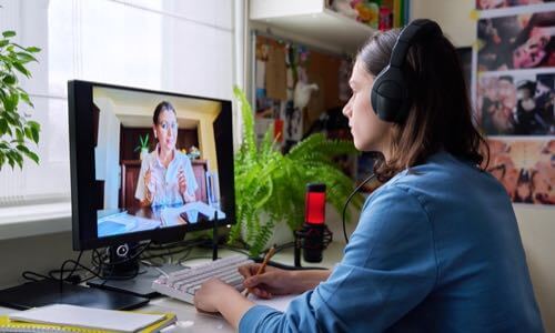 Young woman sitting at a desk wearing a headset & having a virtual meeting on her desktop computer